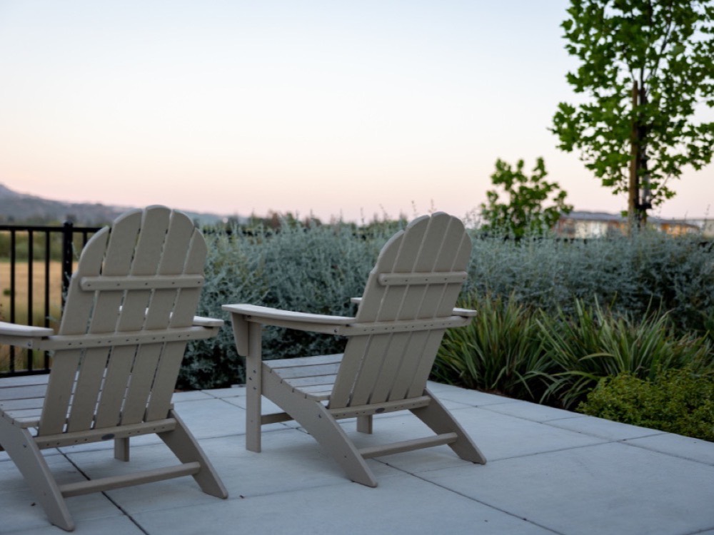 Two Adirondack chairs on a newly laid paver patio bordered by ornamental grasses.